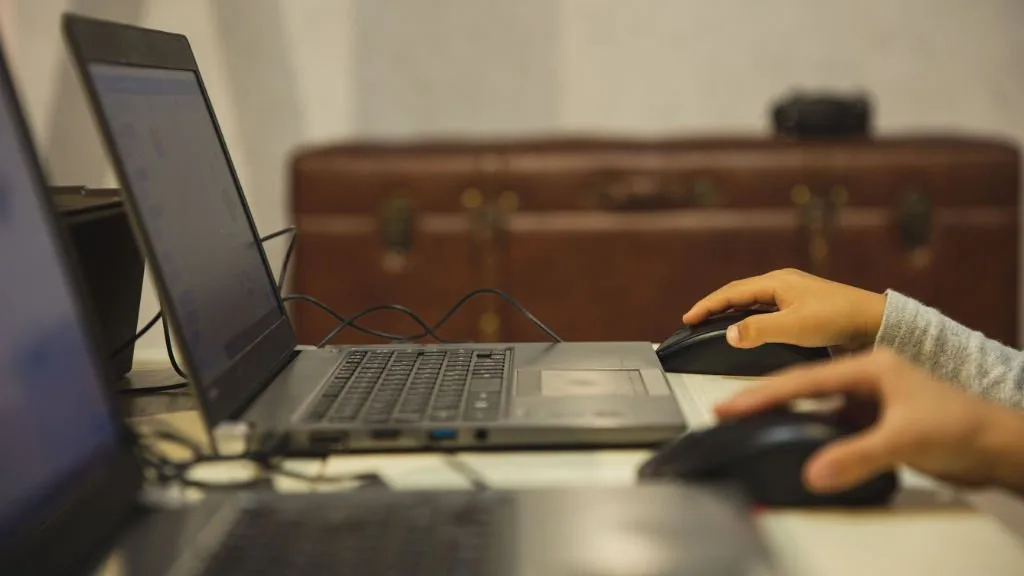 Visão lateral de laptops e equipamentos de TI sendo usados em uma mesa de trabalho.