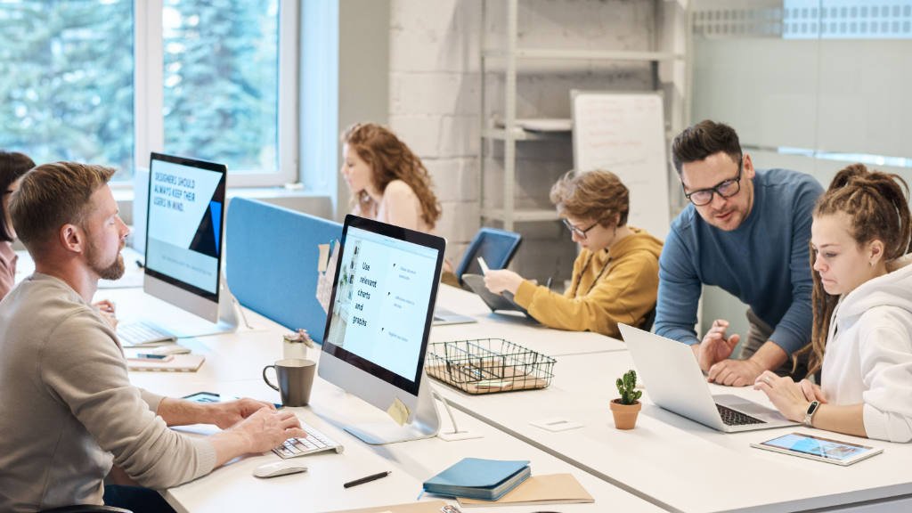 Profissionais em escritório moderno usando notebook e PCs para trabalhar em suas mesas.