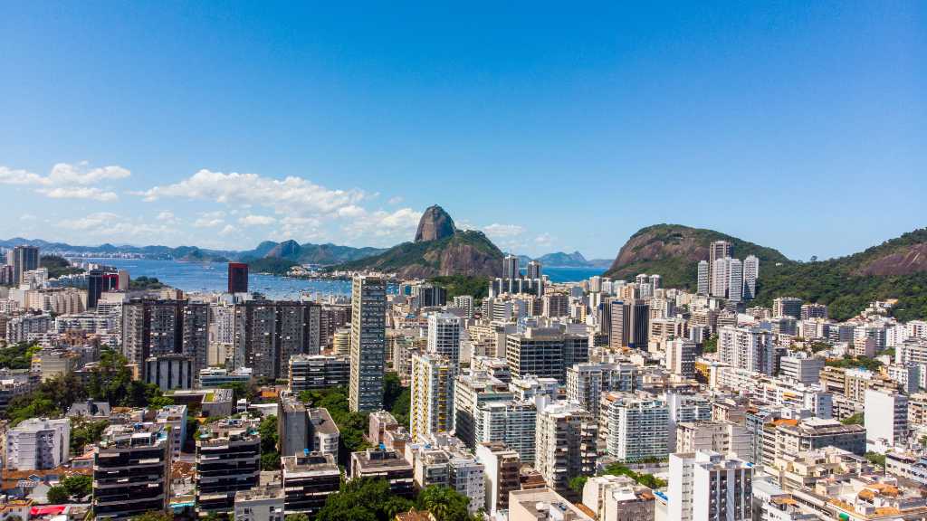 Vista aérea do horizonte do Rio de Janeiro com o Pão de Açúcar sob um céu azul claro.