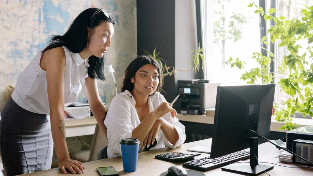 Duas mulheres analisando dados na tela do computador.