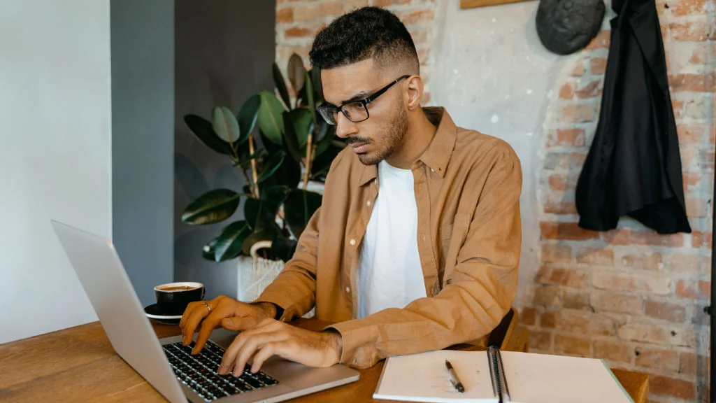 Homem concentrado digitando no computador em mesa de trabalho remoto.
