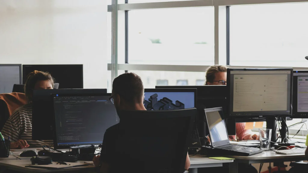 Profissionais trabalhando com programação em computadores em um ambiente de trabalho moderno e iluminado.