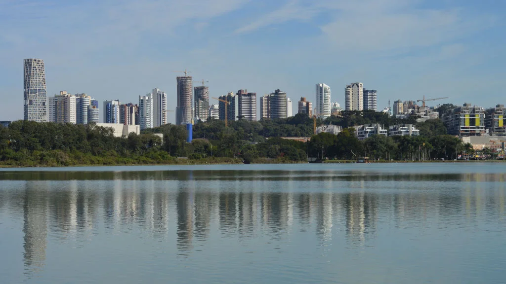 Vista panorâmica do lago no Parque Barigui Curitiba com horizonte urbano e áreas verdes ao redor.