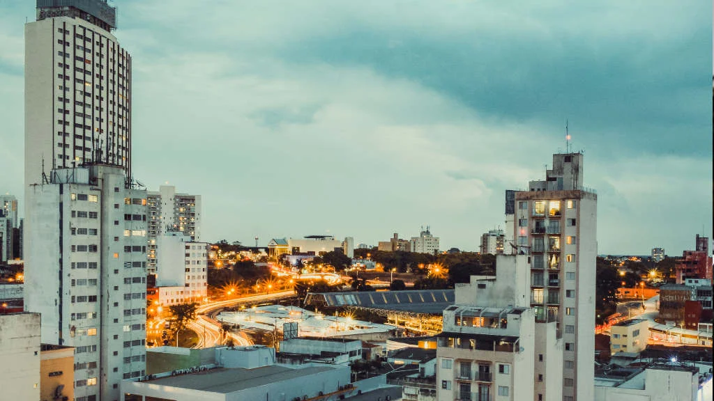 Vista do centro urbano de Campinas ao anoitecer com prédios altos e luzes do trânsito na avenida.