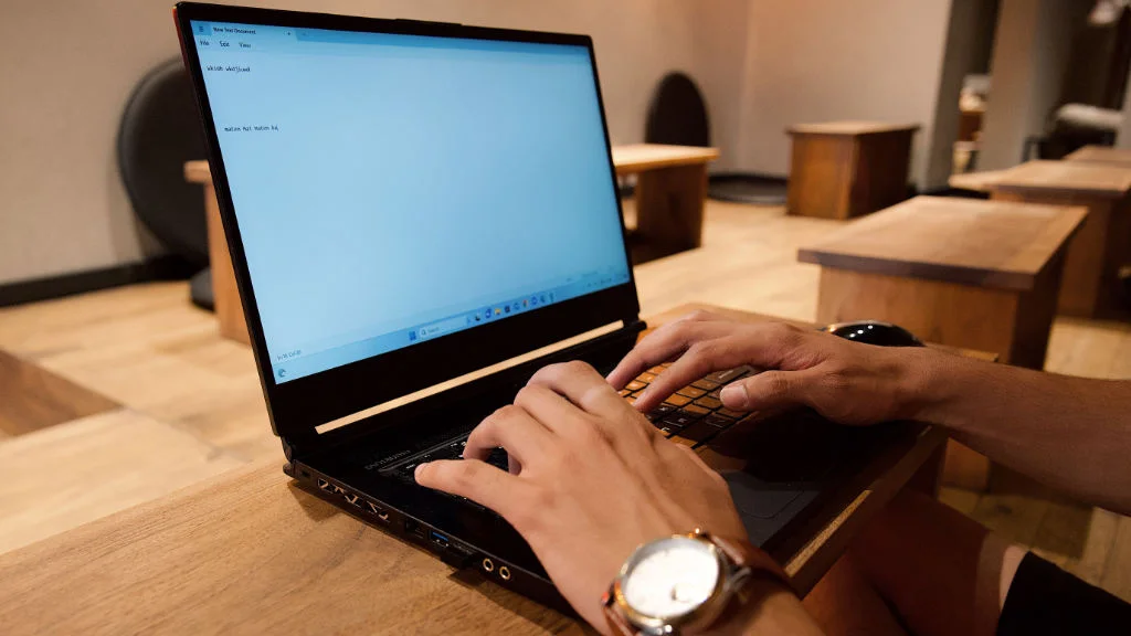 Pessoa trabalhando remotamente no notebook enquanto digita um documento de texto.