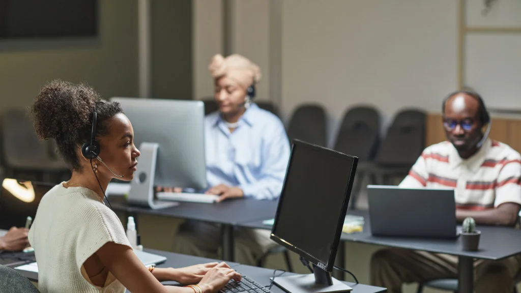 Equipe com headsets trabalhando com computadores em um escritório moderno.