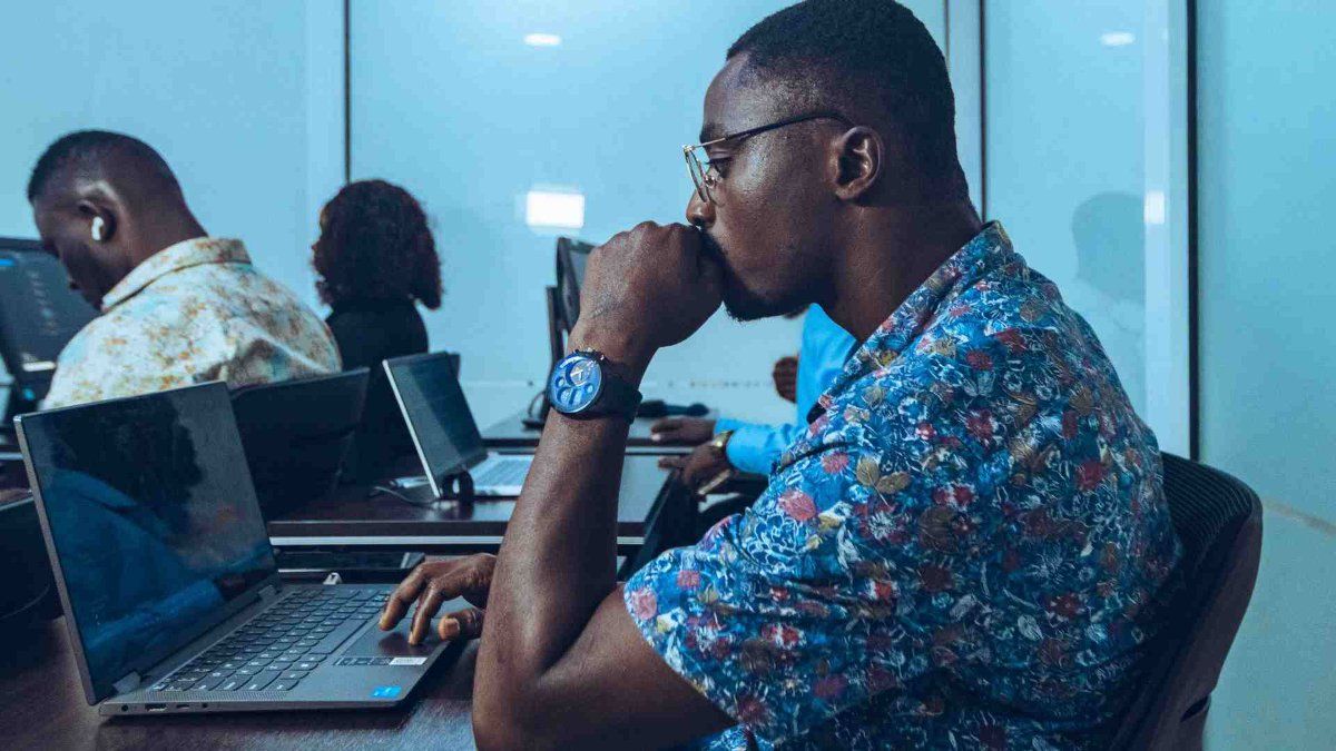 Homem concentrado no notebook em escritório moderno com equipamentos de ti.