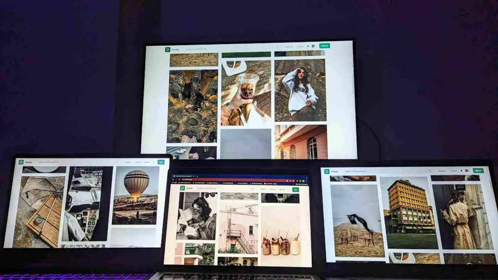 Quatro telas, incluindo notebook e PC para trabalhar, exibindo um banco de imagens em um ambiente com iluminação escura.