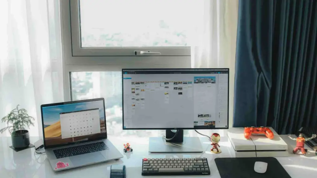 Monitor de computador, notebook e acessórios gamer como equipamentos para home office em um ambiente iluminado.