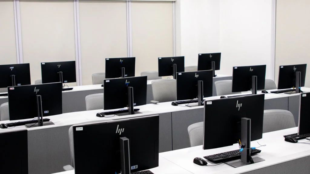 Laboratório de informática moderno com várias bancadas equipadas com computadores e cadeiras organizadas