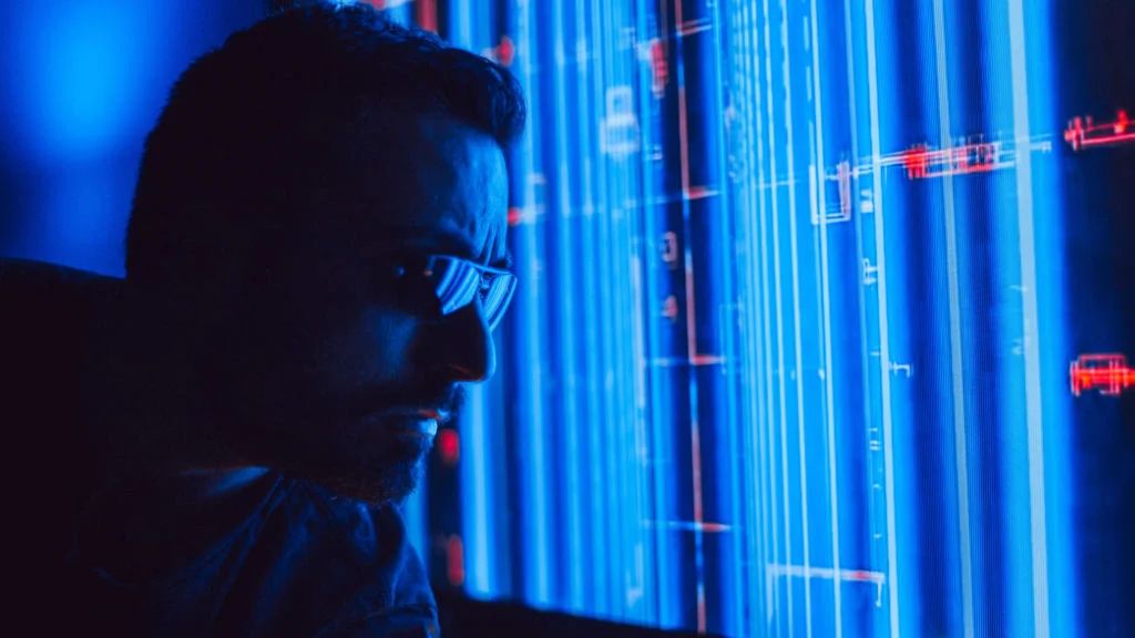 Homem analisando dados digitais em tela vertical com iluminação azul e linhas de código cibernéticas.