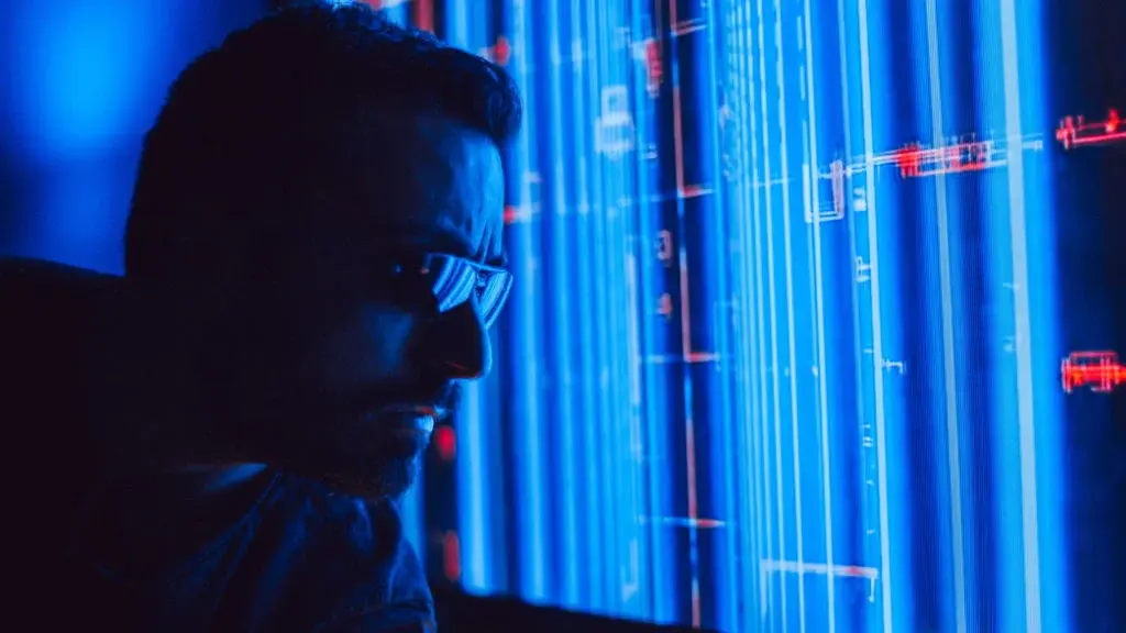 Homem analisando dados digitais em tela vertical com iluminação azul e linhas de código cibernéticas.
